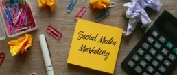 Social Media Marketing steht auf einem Zettel, drumherum Büroklammern und ein Taschenrechner