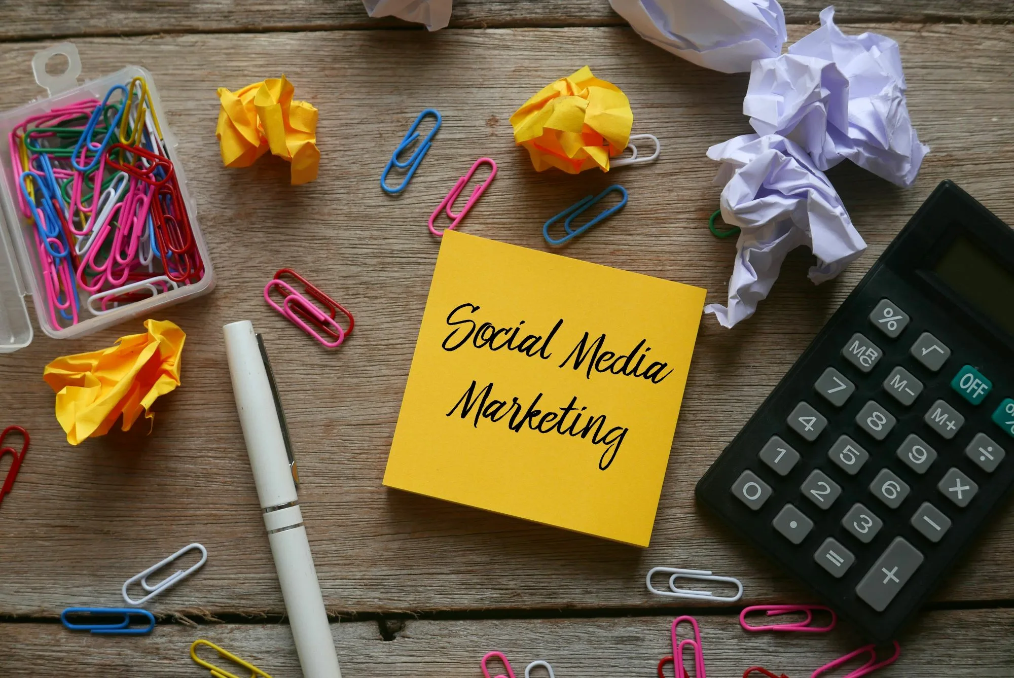 Social Media Marketing steht auf einem Zettel, drumherum Büroklammern und ein Taschenrechner