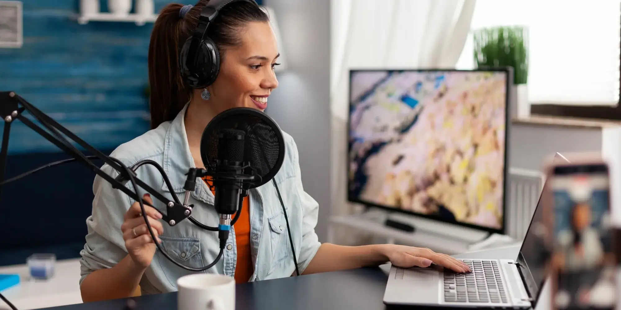 Frau produziert einen Podcast an einem Schreibtisch, mit blauem Studio-Hintergrund
