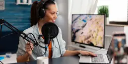 Frau produziert einen Podcast an einem Schreibtisch, mit blauem Studio-Hintergrund